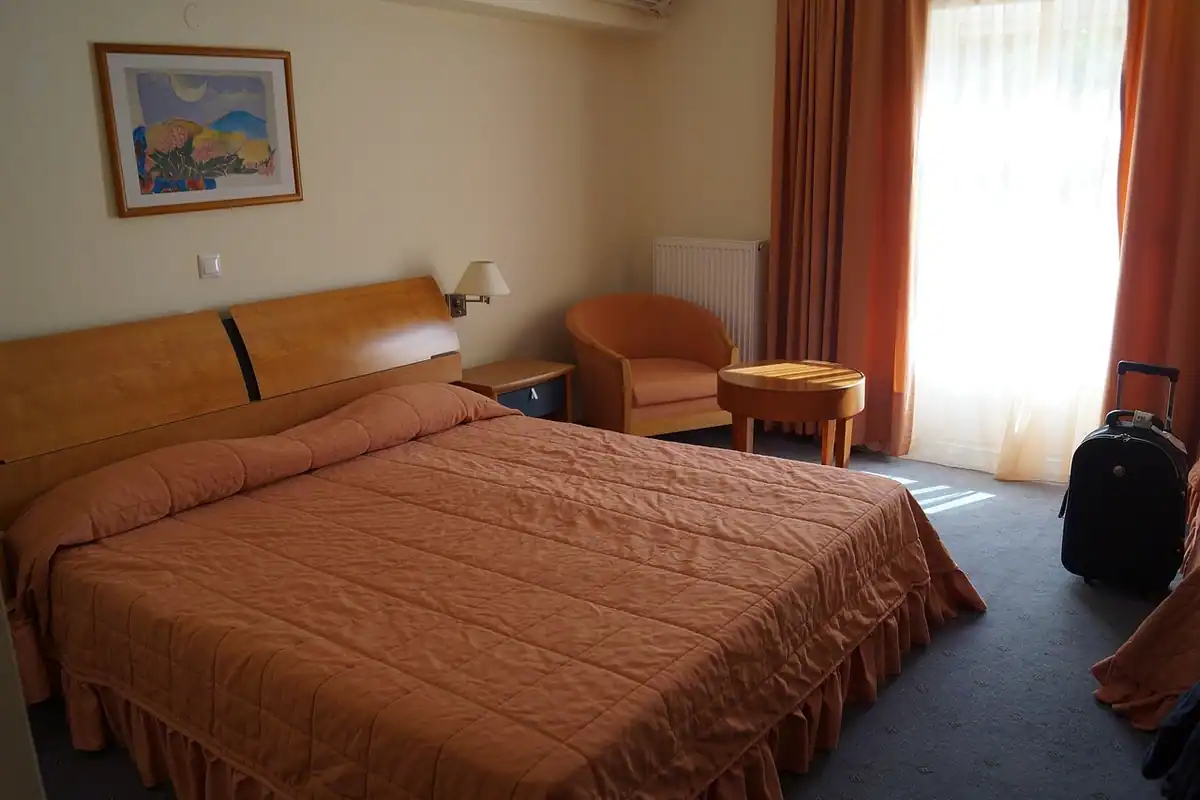Pat dublu cu așternuturi și pled într-o cameră de hotel, pregătită pentru odihnă
