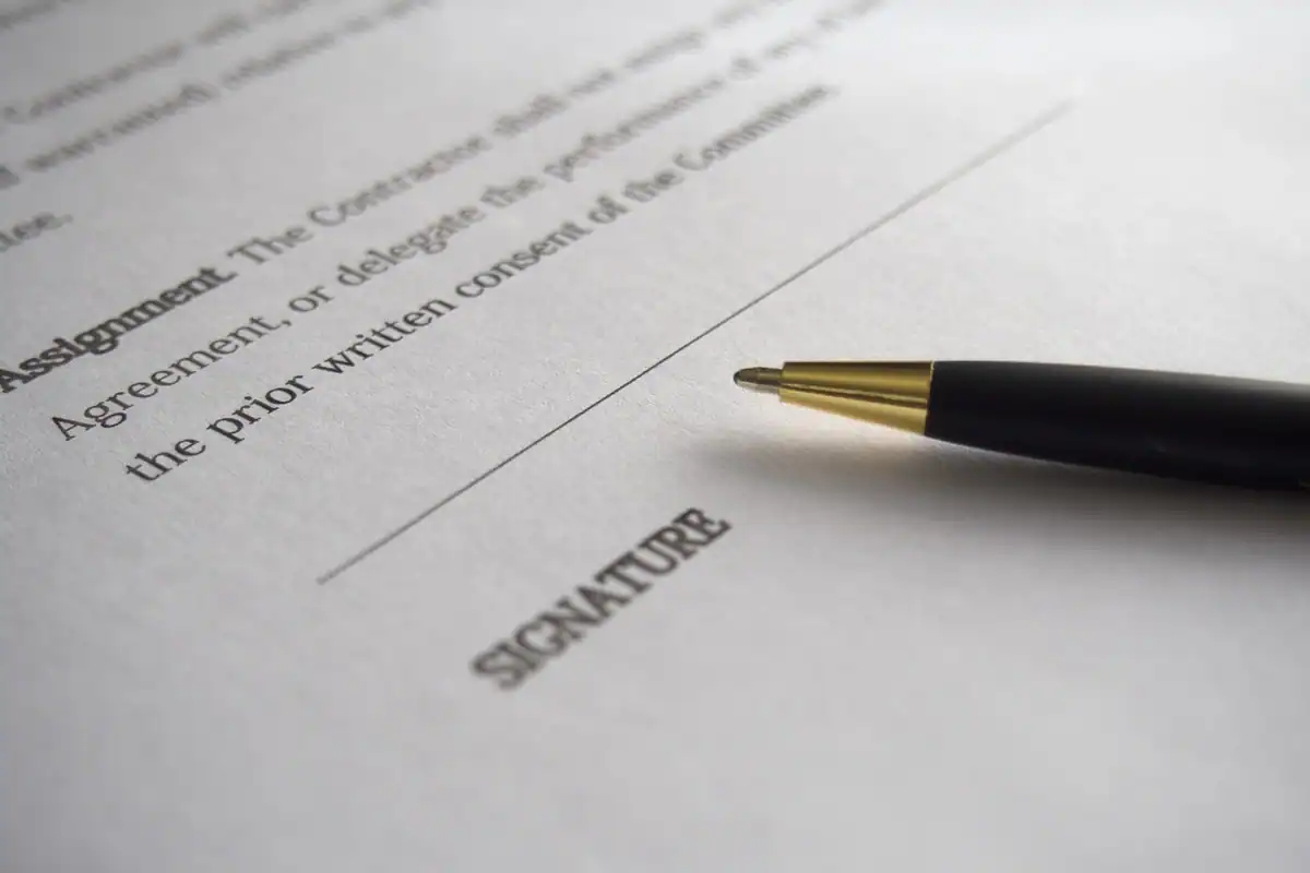 Mână care semnează un contract pe hârtie, cu documentele pregătite pe masă