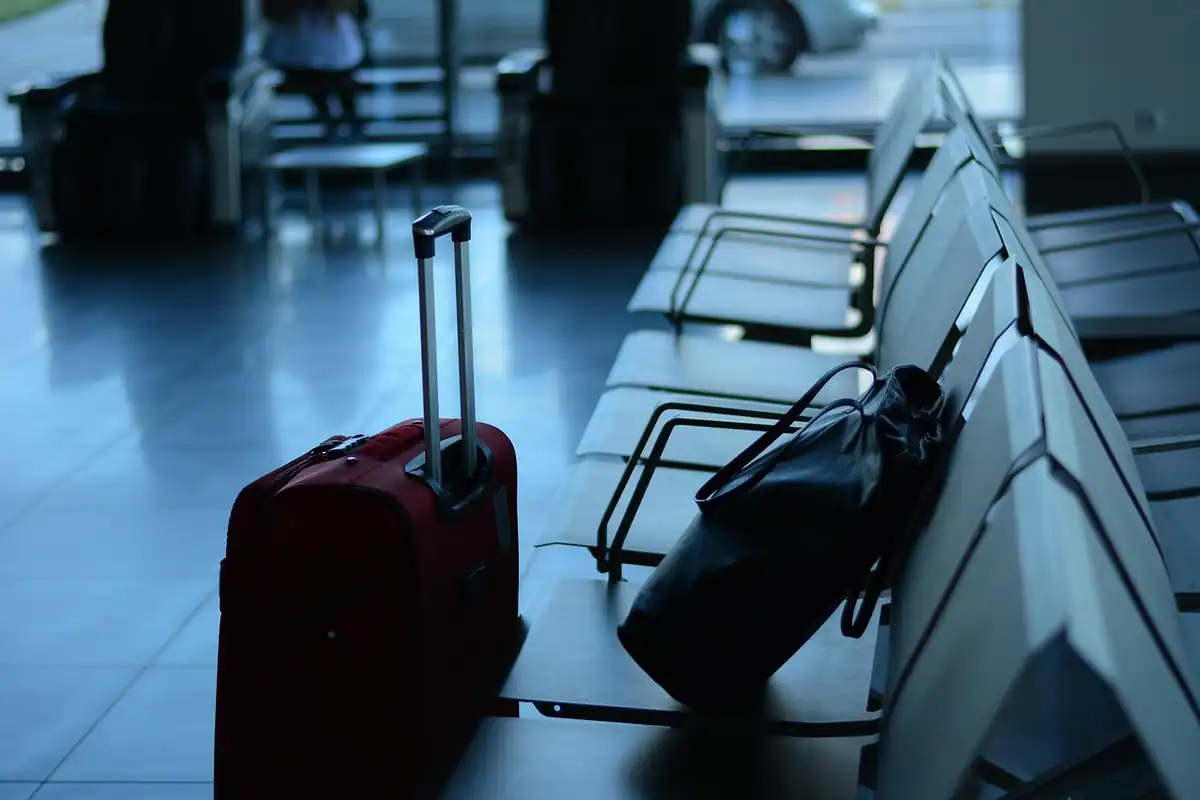 Valiză roșie și genți lângă scaunele unui terminal de aeroport