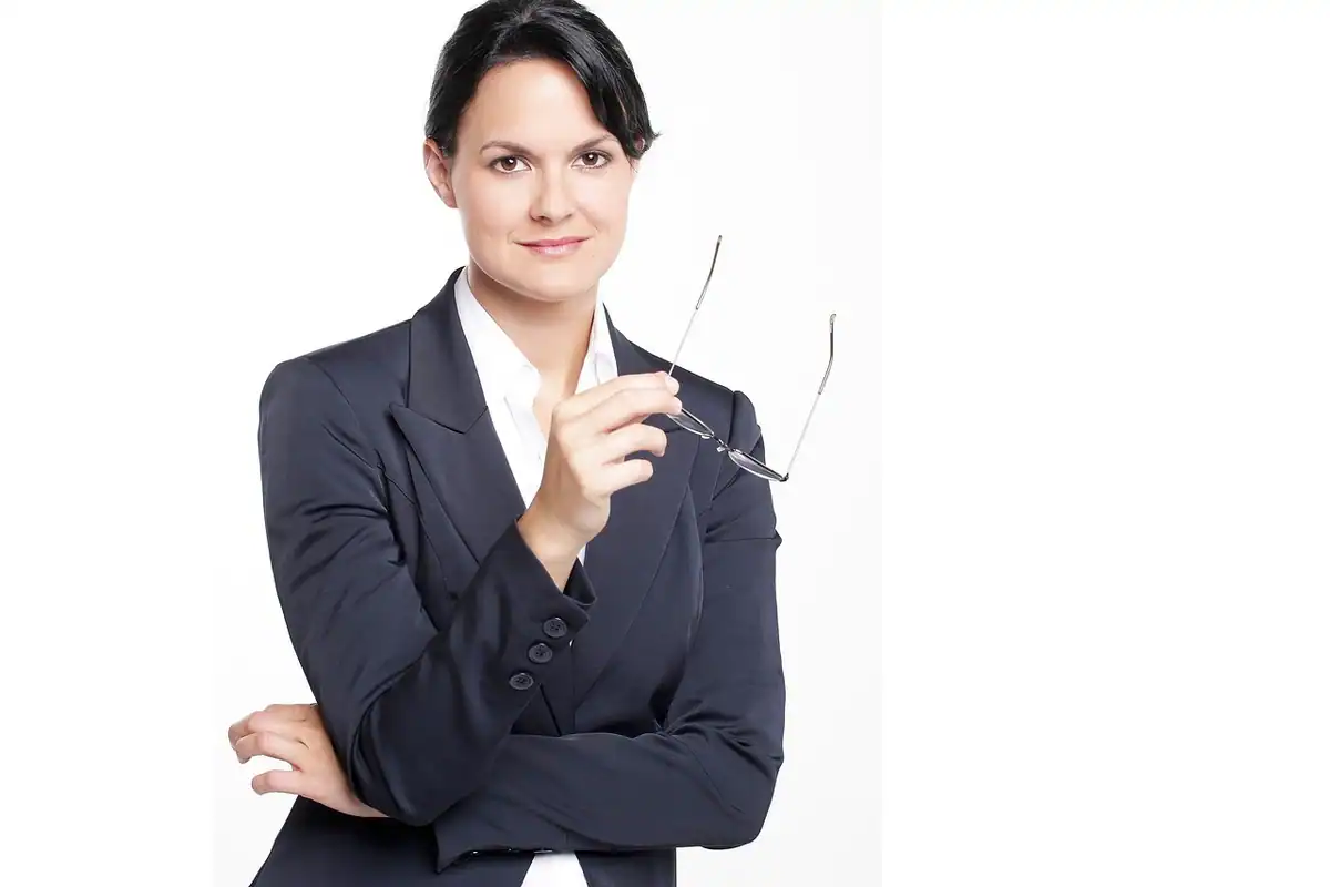 Funcționară în costum închis stă cu brațele încrucișate, pe fundal alb