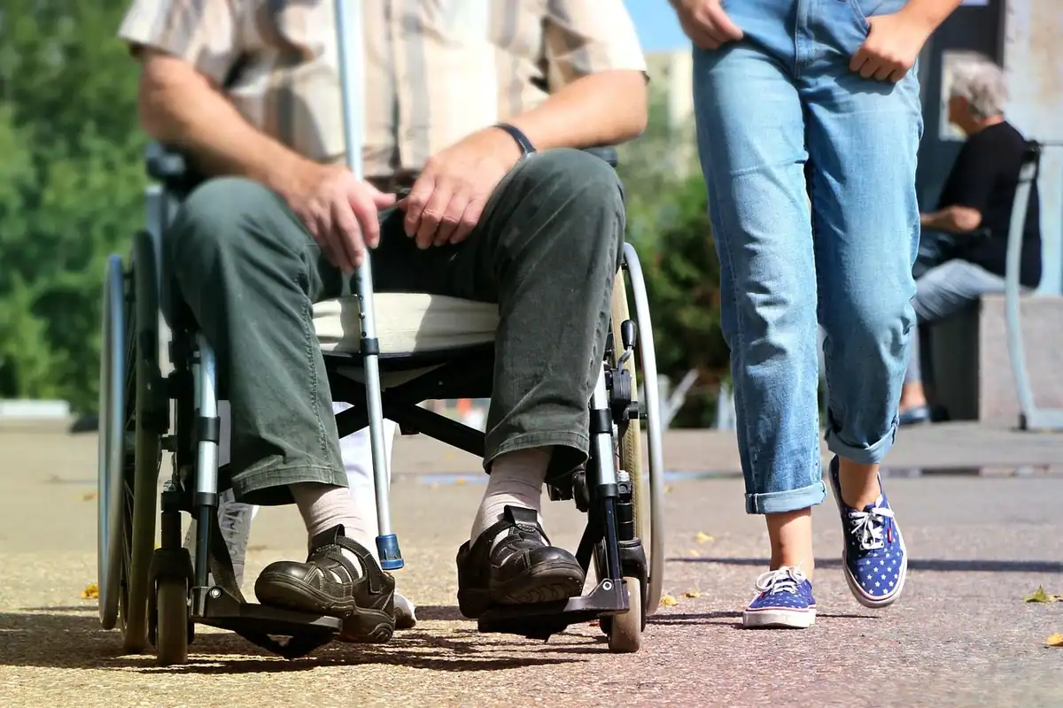 Persoană în scaun cu rotile alături de un trecător, pe trotuar