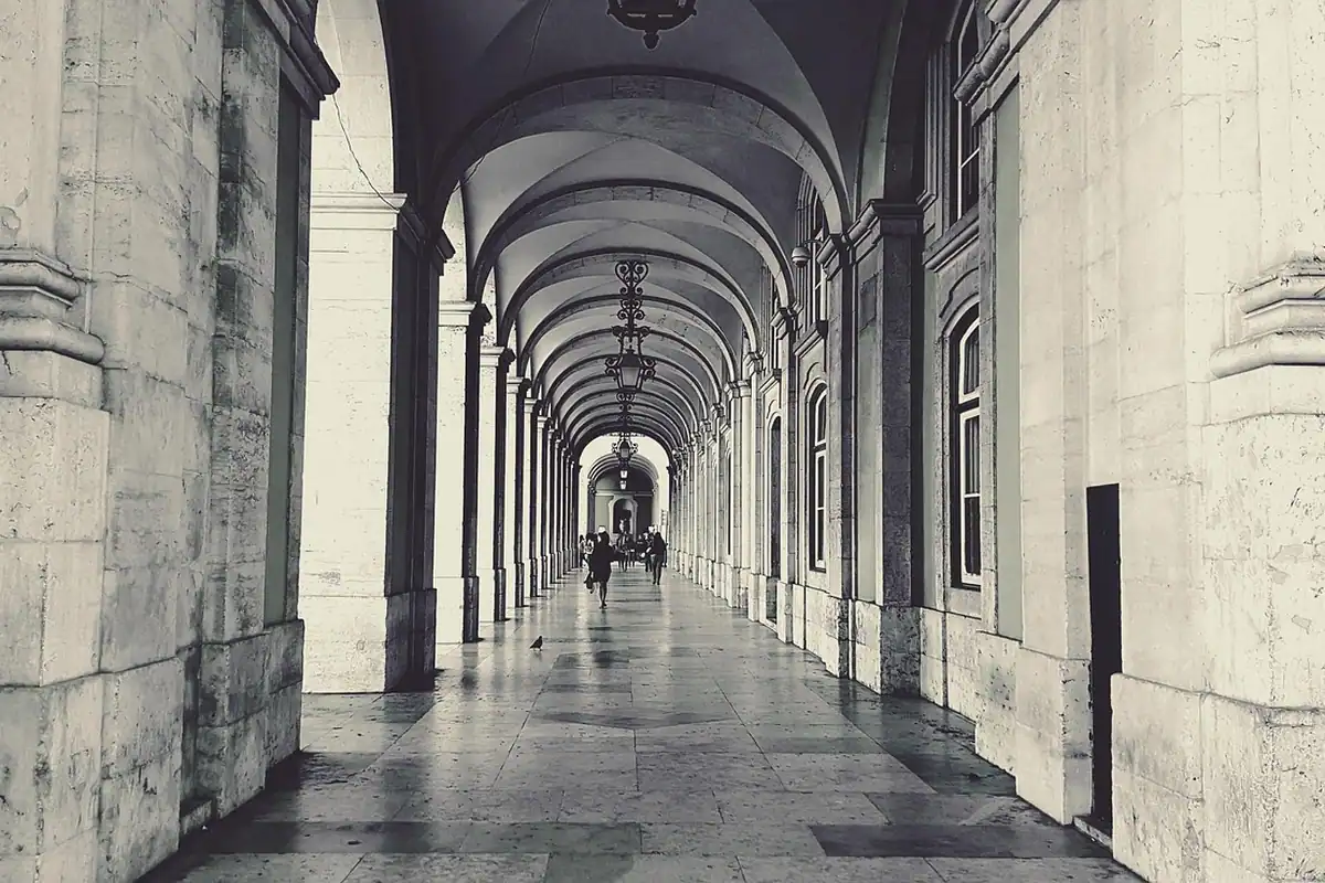 Coridor cu arcade și coloane din piatră, pe un pavaj de piatră, într-un oraș istoric
