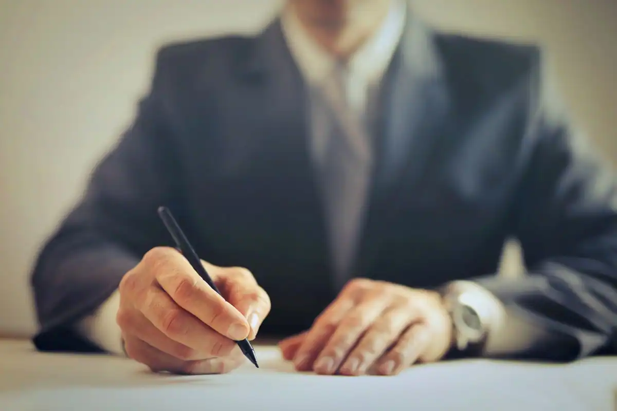 Mâna unei persoane în costum semnează un document cu pixul