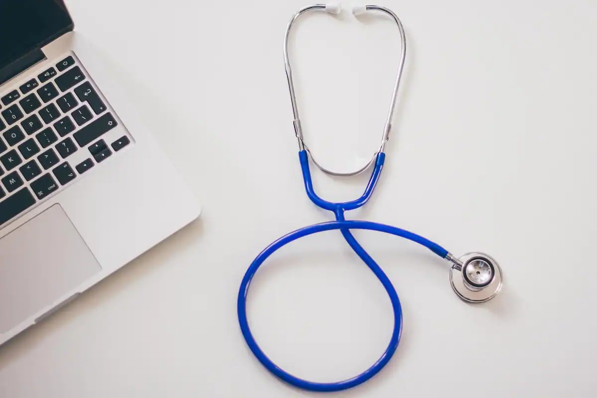 Stetoscop albastru lângă un laptop, pe biroul unui medic de familie