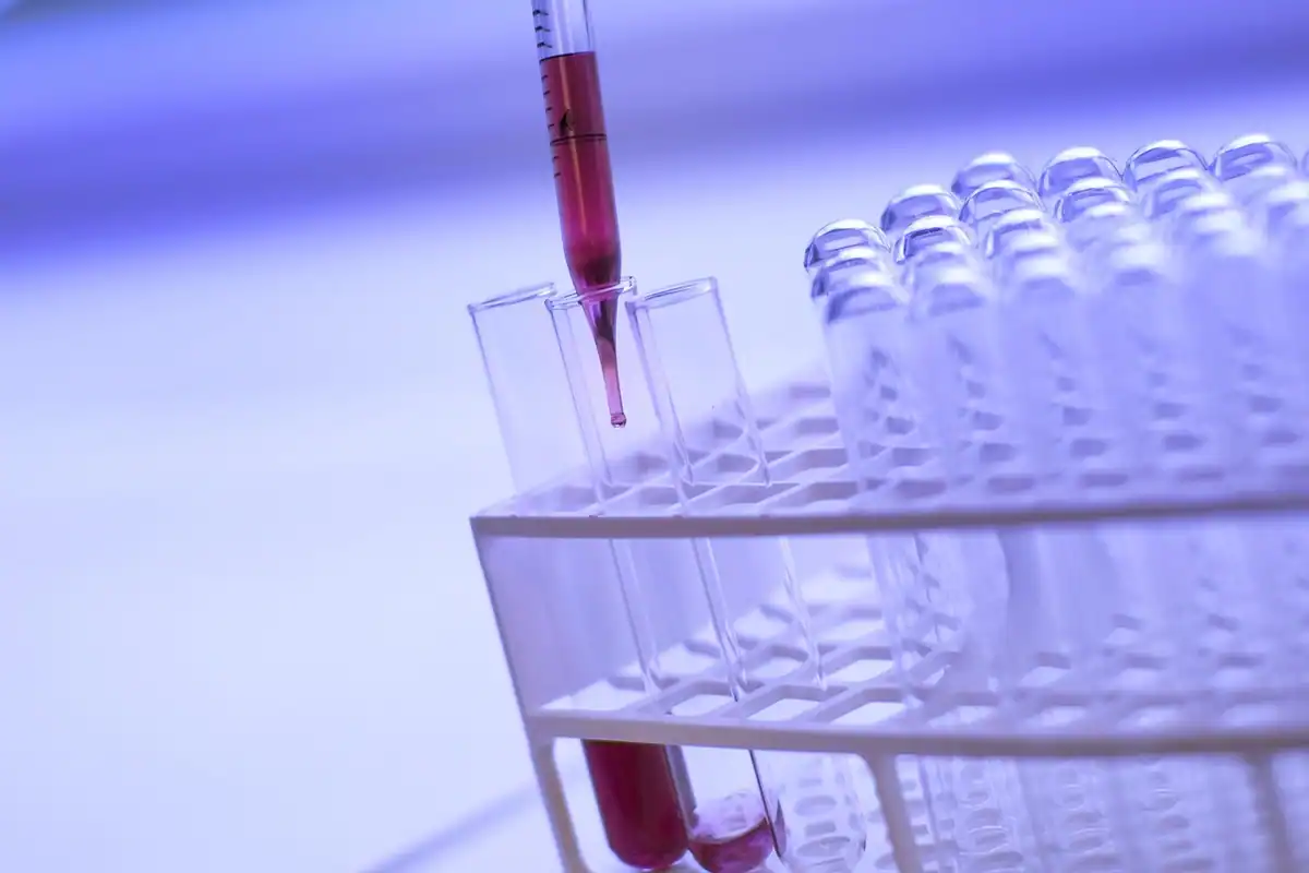 Eprubete și pipetă cu lichid roșu într-un laborator, în nuanțe violete