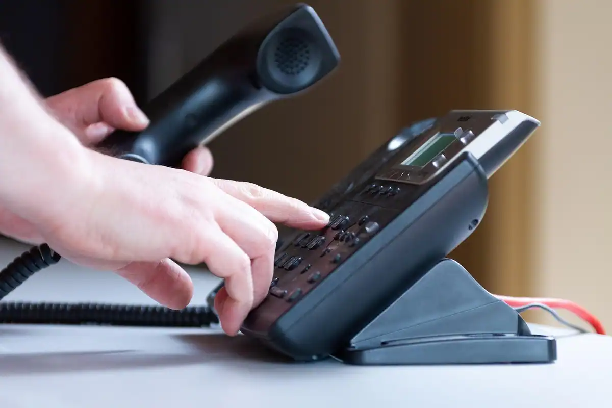 Mână formează un număr pe un telefon fix de birou