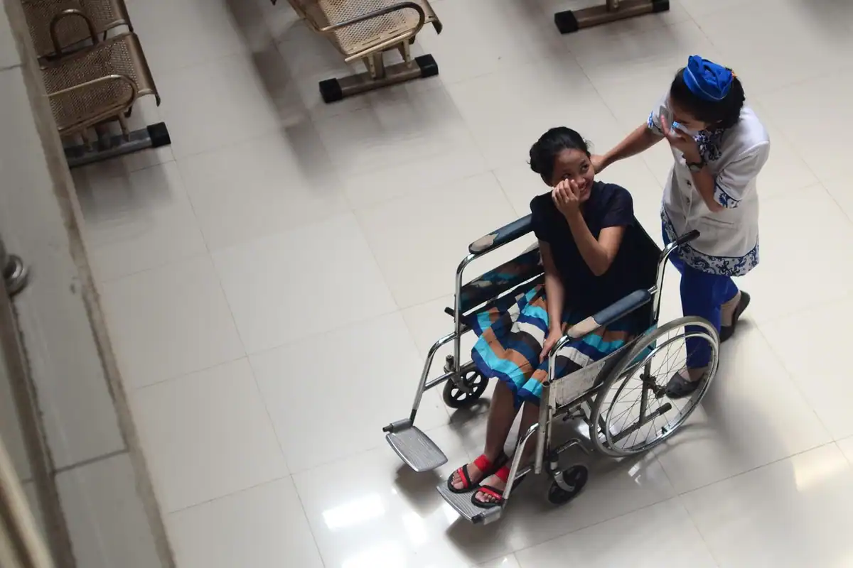 Asistent împinge un pacient în scaun cu rotile pe holul unui spital