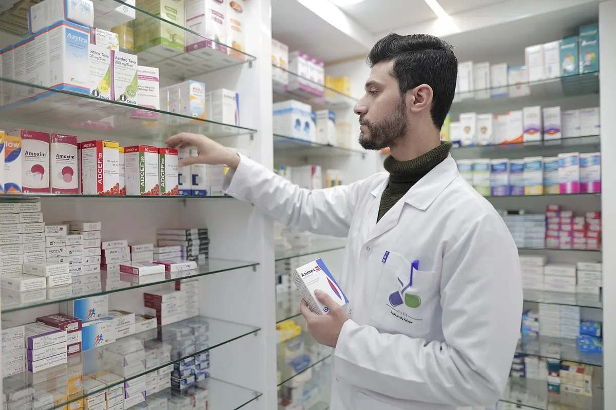 Farmacist în halat alb caută un medicament pe rafturile farmaciei