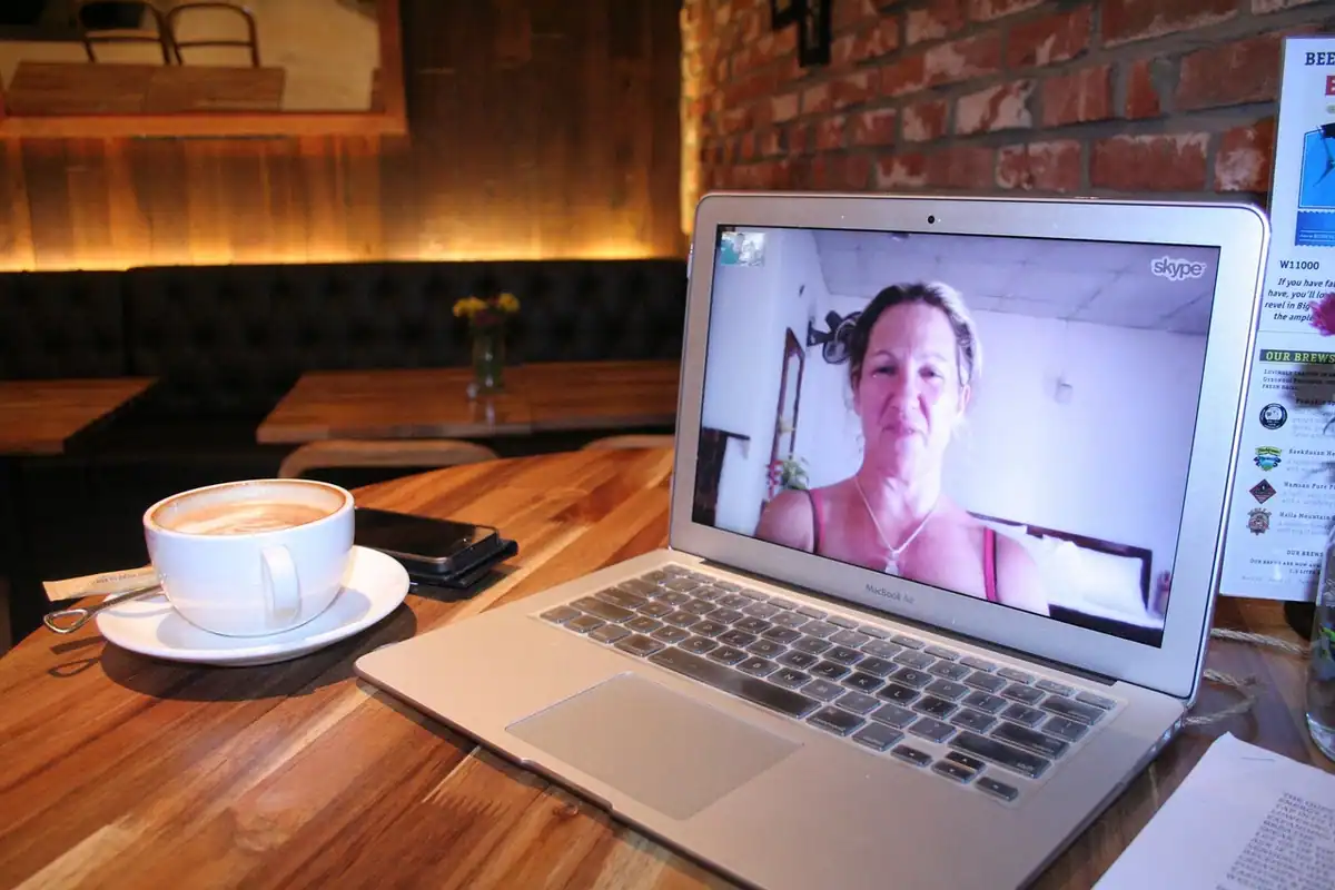 Apel video pe laptop, lângă o cafea, într-un local cu pereți de cărămidă