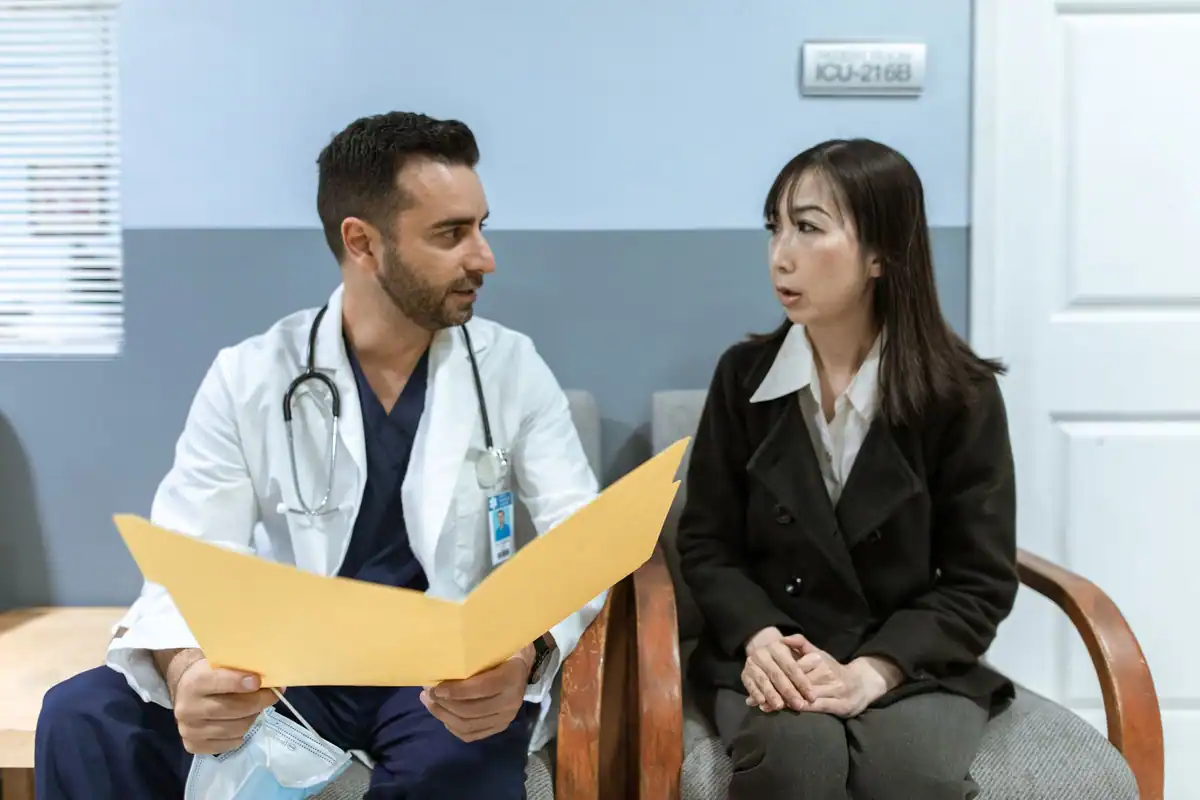 Medic cu dosar galben discută cu o pacientă, pe scaunele din cabinet