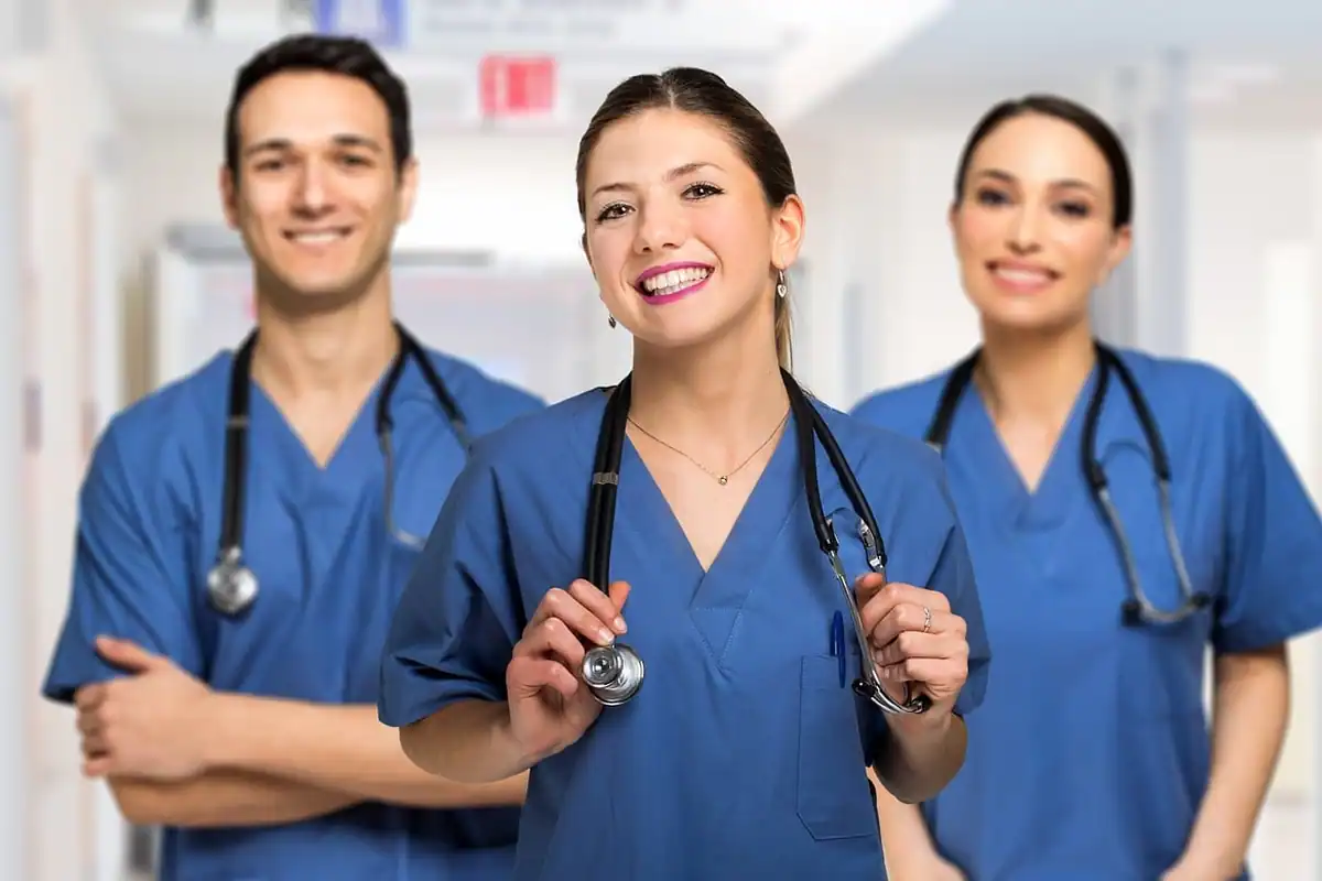 Trei membri ai personalului medical în uniformă albastră zâmbesc spre cameră
