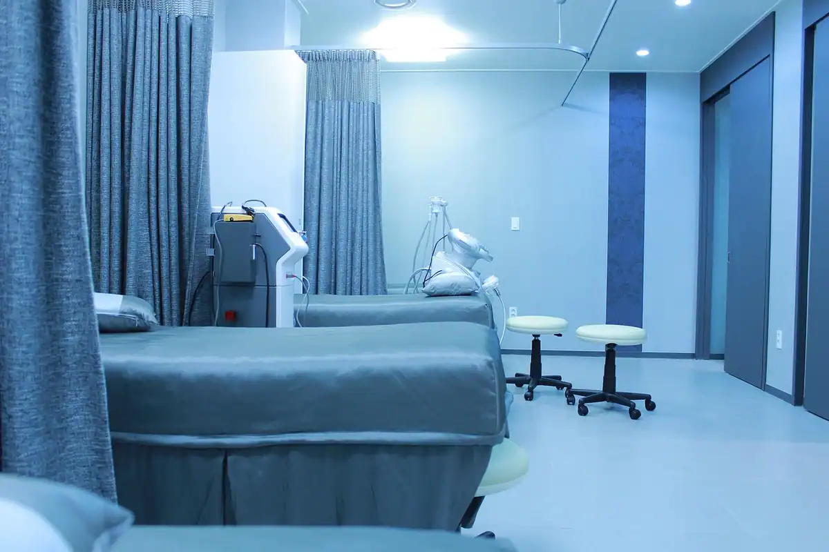 Salon de spital cu paturi albastre, perdele și scaune pe roți