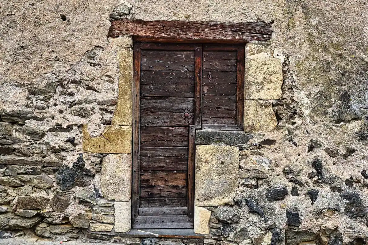 Ușă veche într-un perete rustic de piatră, cu o intrare simplă și zid din pietre